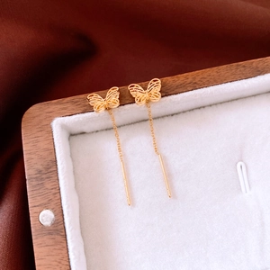 Macro detail of 18K gold plated butterfly long chain earrings on a wooden jewelry box