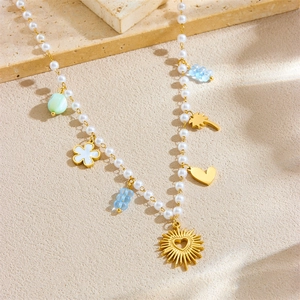 Mode Perlenkette mit goldenem Herz, Palme und Blumenanhängern auf einer Steinfläche
