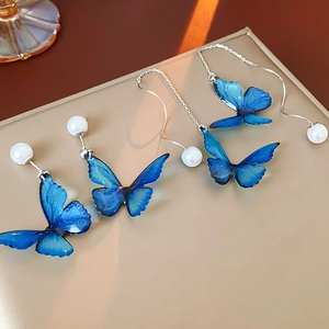 Macro detail of blue butterfly earrings with white pearls on a light gold surface