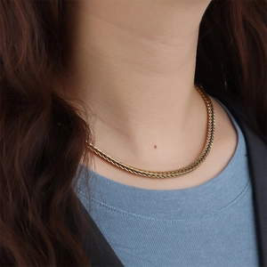 Detail of a golden wheat chain necklace featuring a textured woven design on model neck
