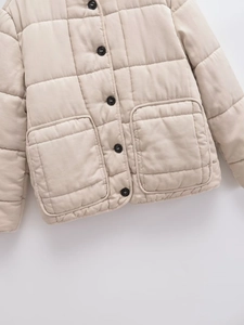 Detail of beige quilted jacket featuring black buttons and large square pockets