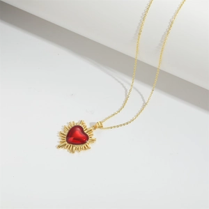 Close-up of golden necklace featuring a sunburst design with a red heart-shaped gemstone