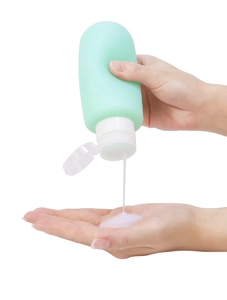Detailed view of a mint green silicone travel bottle dispensing white lotion into a hand