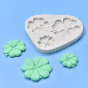 Three-cavity four-leaf clover silicone mold with green fondant shapes on blue background