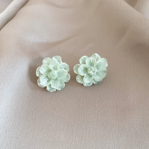 Close-up of pale green flower earrings with layered resin petals on champagne fabric
