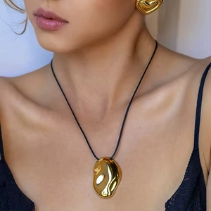 Golden irregular pendant necklace with black cord and heart earrings set on model