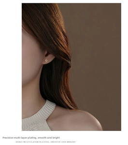 Close-up of a teardrop-shaped gold-plated stud earring worn on a model's ear lobe