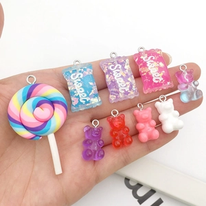 Handheld view of colorful resin candy charms, glitter bears, and lollipops with metal loops