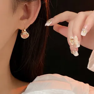 Golden vintage round earrings with red letter M inlay shown on model ear