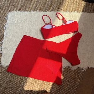Flat lay of red ribbed three-piece bikini set with matching mini skirt on woven rug
