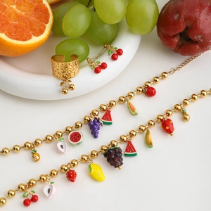 Detailed set of gold fruit jewelry with enamel cherry and grape charms on white backdrop