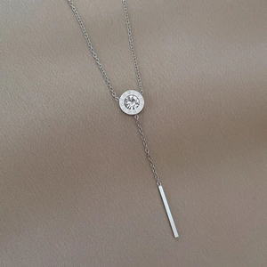 Detail of silver Y-necklace featuring a Roman numeral ring with crystal and tassel bar