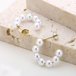 Macro shot of C-shaped 18K gold-plated earrings with pearls on beige textured stone
