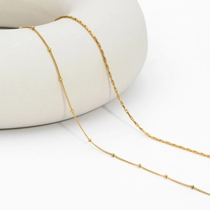 Detail of gold beaded and box chain necklaces displayed on a white professional prop