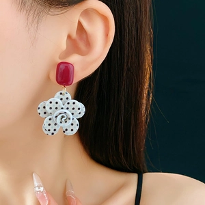 Détail de boucles d'oreilles rétro à fleurs blanches à pois noirs et clous carrés rouges
