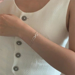 Detailed view of a minimalist silver knot bracelet on model wrist with tweed background
