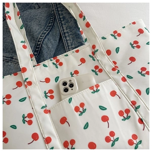 Close-up of white tote bag with red cherry prints showing front pocket and mobile phone