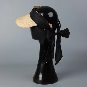 Detail of sun visor with straw brim and black ribbon tie featuring pearl accents