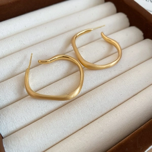 Close-up of matte gold irregular square earrings displayed on a beige fabric jewelry box