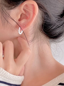 Detail shot of a minimalist silver U-shaped earring worn by a model in soft lighting
