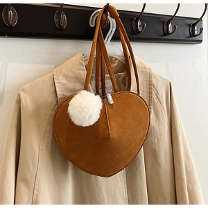 Detail einer hellbraunen herzförmigen Wildledertasche mit weißem Fellanhänger und Riemen