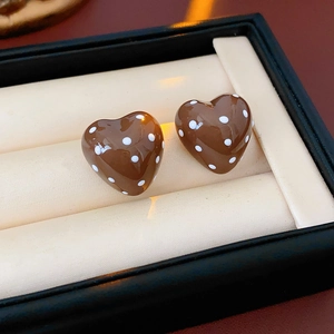Detail of brown heart earrings with white polka dots on a soft beige cushion