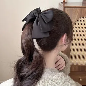 Detail of a large black satin bow banana clip worn on a low ponytail in a French style