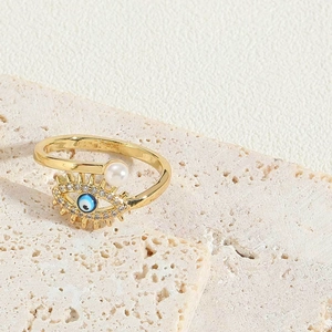 Close-up of golden Evil Eye ring with micro-pave crystals and a white pearl detail