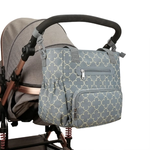 Gray diaper bag with yellow clover patterns attached to a stroller handlebar