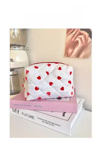 Close-up of white quilted makeup bag featuring red heart patterns and heart zipper pull