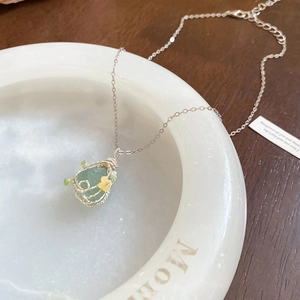 Detail of wire-wrapped light green stone pendant on a silver chain over marble