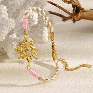 Détail du pendentif soleil en or 18K sur bracelet tissé rose et blanc sur corail