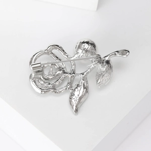 Silver rose brooch pin with rhinestone details and metal back clasp on white background