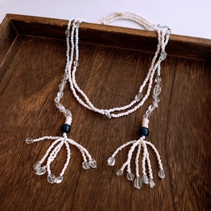 Detailed view of bohemian beaded necklace with white resin beads and glass tassel on wood