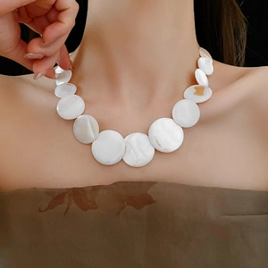 Detailed view of a geometric white shell pendant on a gold necklace worn by a model