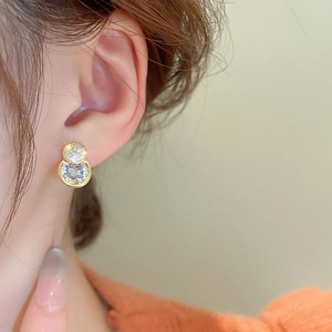 Macro close-up of zircon double hoop gold earrings worn by a model on a beige backdrop