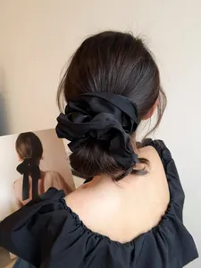 Close-up of premium black satin scrunchie with soft sheen and elegant pleated texture