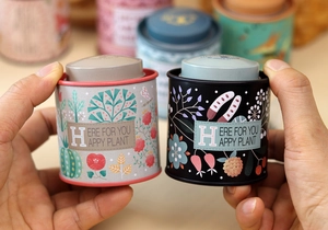 Close-up of grey and black tinplate tea canisters with floral plant patterns