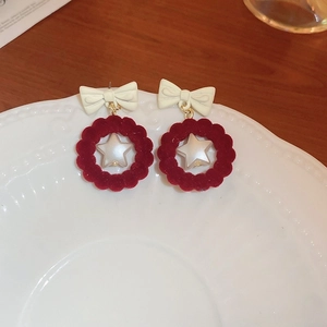 Détail de boucles d'oreilles en velours rouge avec nœud blanc et étoile sur céramique