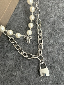 Detail of double-layer silver chain necklace featuring a pearl strand and metal padlock