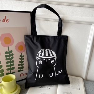 Detail of black canvas tote bag featuring a white cartoon cat print in a lifestyle setting