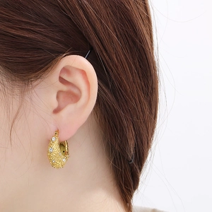 Détail d'une boucle d'oreille en U dorée avec texture tressée et strass brillants
