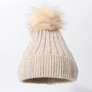 Winter knitted beanie with colorful rhinestones and a fluffy faux fur pompom in cream