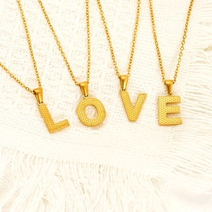 Golden titanium steel LOVE letter necklaces with textured pendants on white fabric