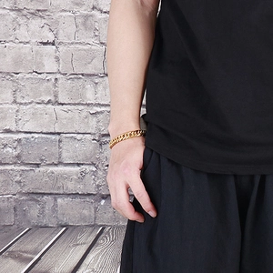 Men's golden cuban link bracelet in bold hip-hop style worn by model on brick wall background