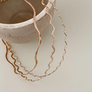 Close-up of polished gold wavy alloy double headband on a minimalist ceramic base