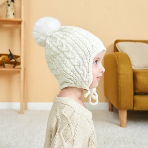 Detailed knit pattern and soft plush pompom on a cream white baby earflap winter hat