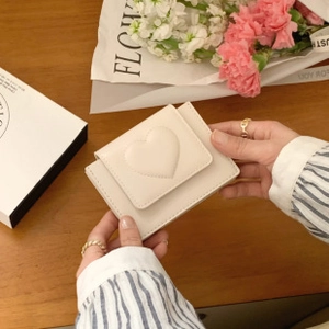 Close-up of off-white faux leather mini wallet with stitched heart detail and flap closure