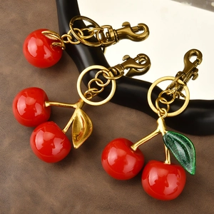 Three red cherry resin keychains with gold metal leaf and ring on leather surface