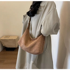 Brown suede hobo bag shown as a shoulder bag on a model in a minimalist indoor setting